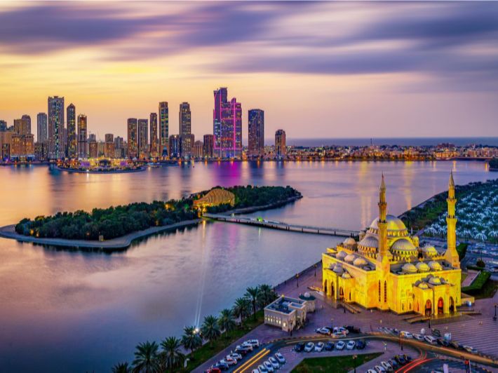 الشارقة ليلاً ، بحر ومسجد واضاءة الأبنية الجميلة تعكس على البحر، والمسجد يعكس جمال العمارة الإسلامية في الإمارة ضمن مشهد يعكس هدوء وسحر السياحة الليلية في الشارقة.